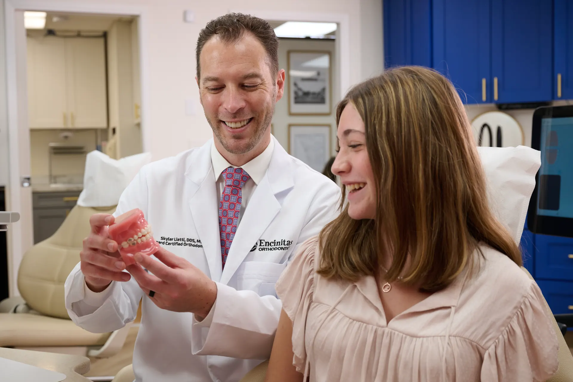 Dr. Liatti showing a demonstration model of braces to a smiling teenage patient