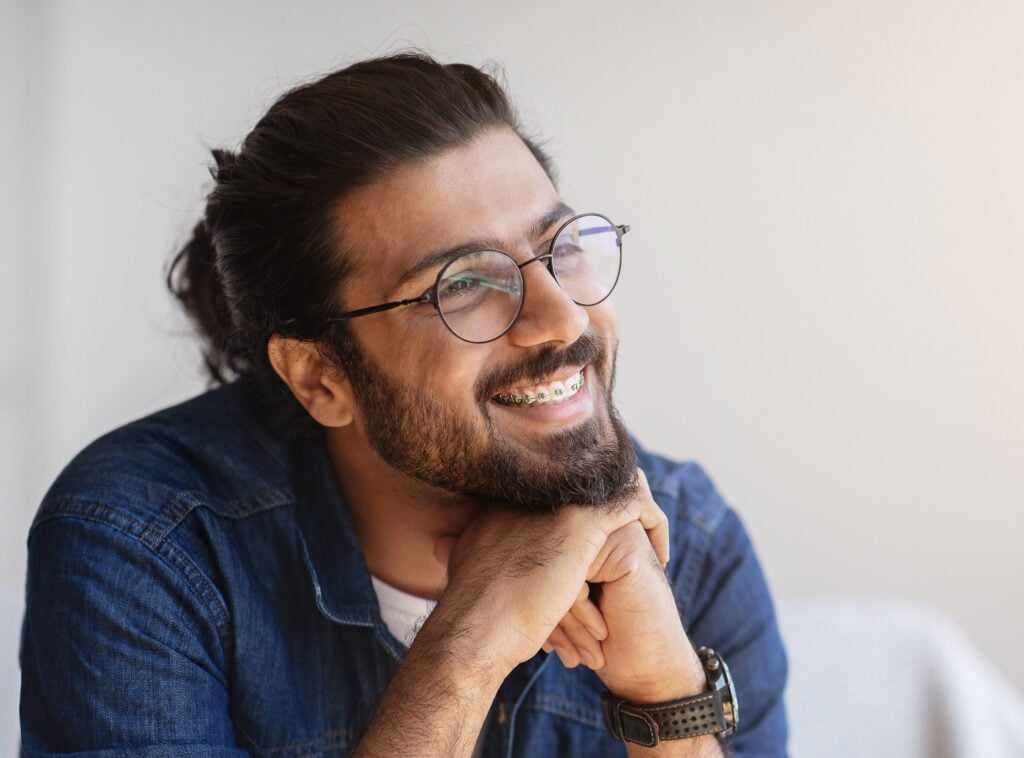 A bearded man wearing glasses smiling with metal braces on his teeth