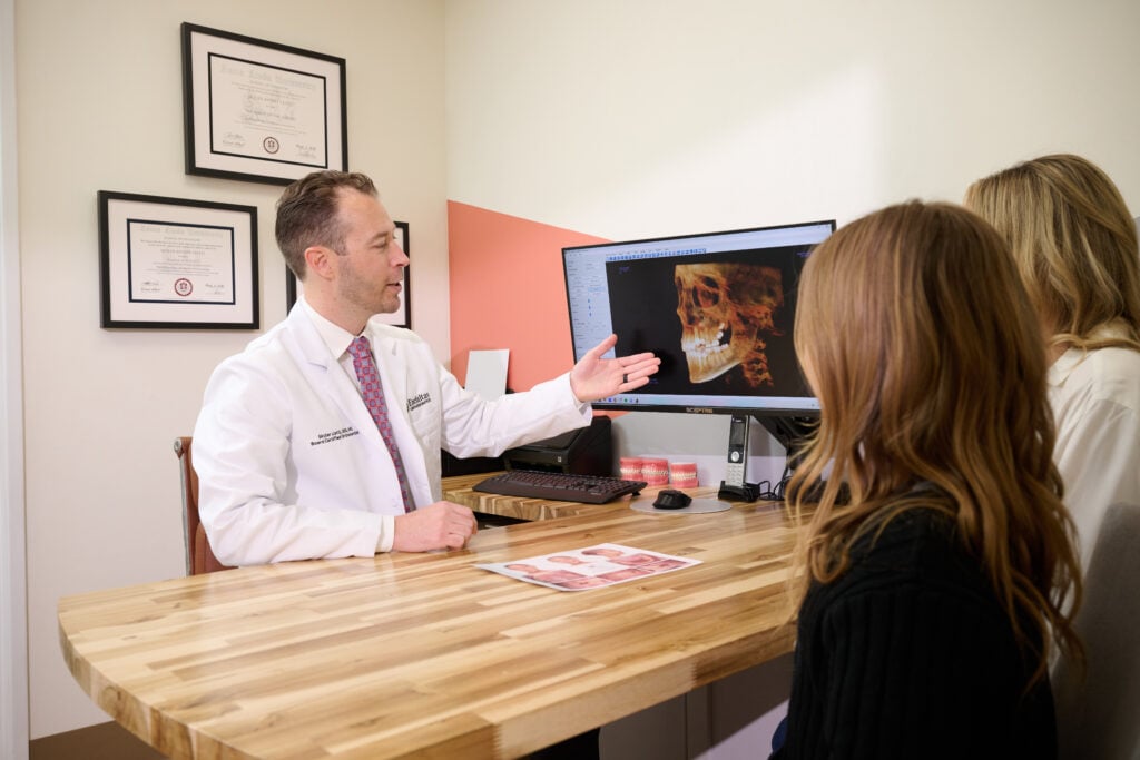 Dr. Liatti pointing to a 3D skull scan on a monitor while a patient and her parent look on