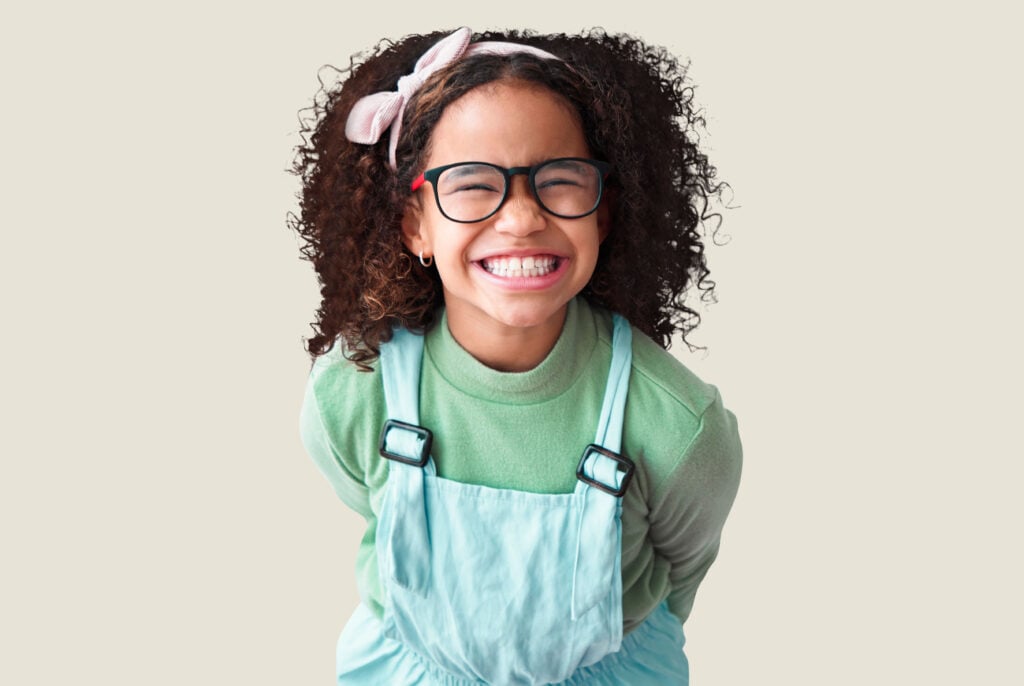 A smiling young girl with glasses and a headband