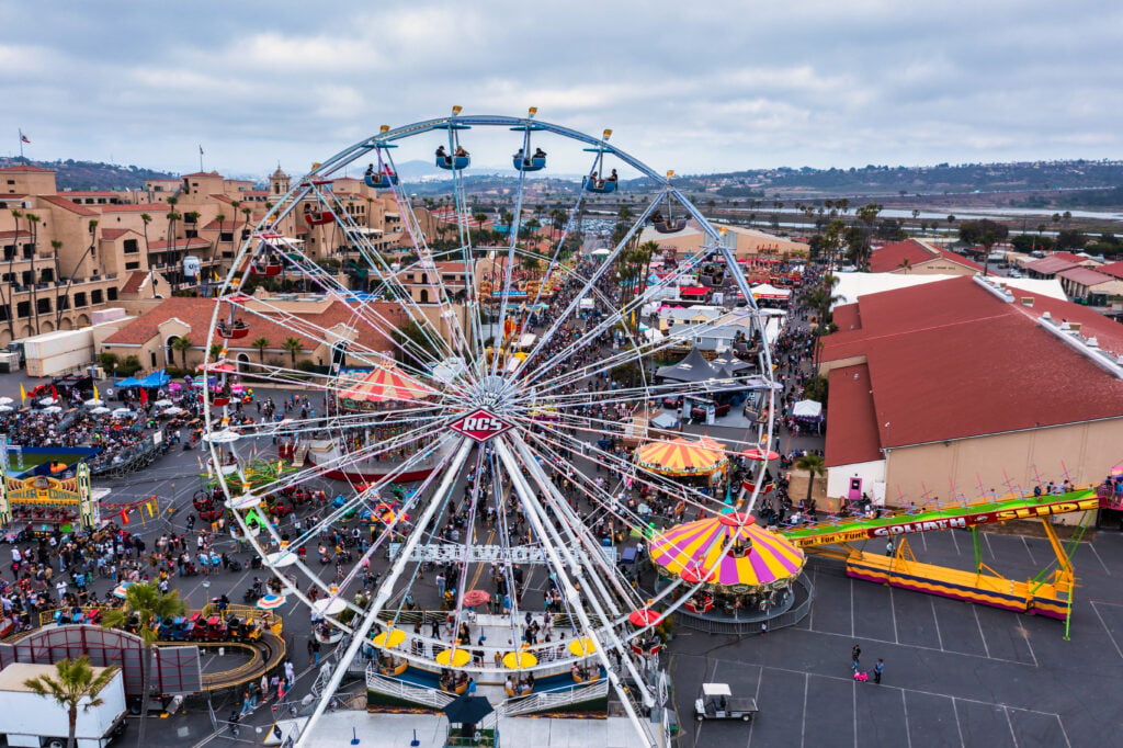 An aerial view of the Del Mar Fairgrounds at fair time, with a Ferris wheel and midway crowds